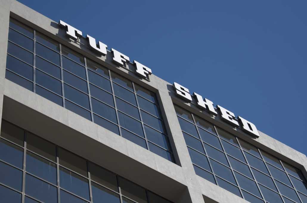 Exterior photo of Tuff Shed's headquarters, taken from the street aimed up showing the giant letters and the top five floors of the building against a blue sky.