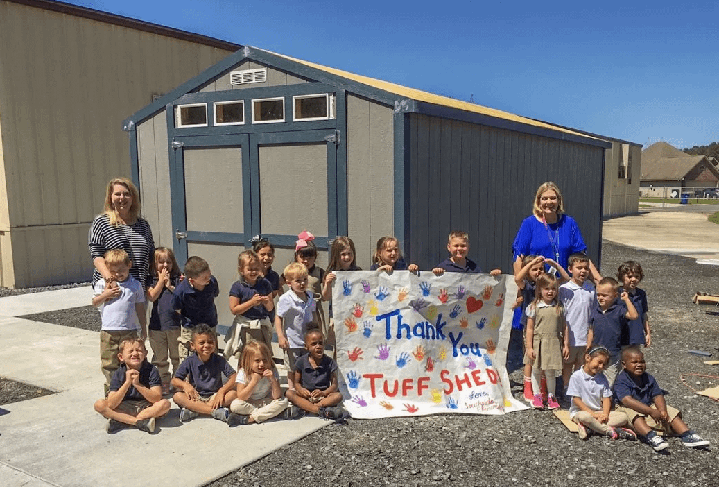Group of South Side Elementary Children plus two adults holding a sign that says Thank you Tuff Shed stand in front of a Premier Ranch, exterior