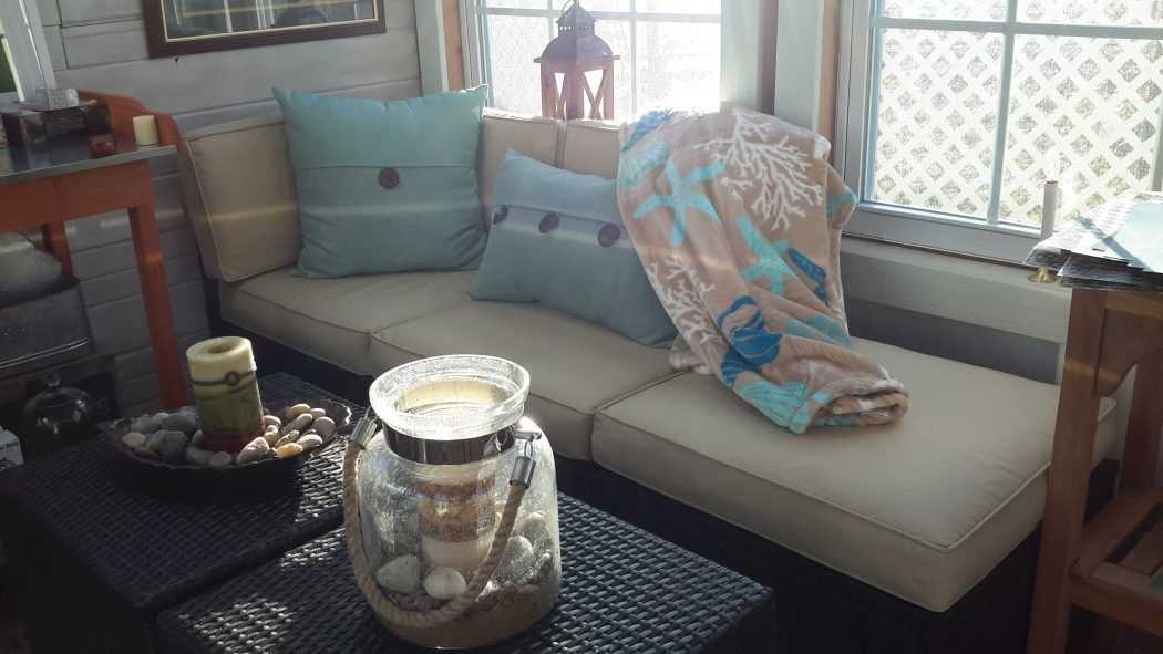 A couch with pillows and decor for a she shed in someones backyard.