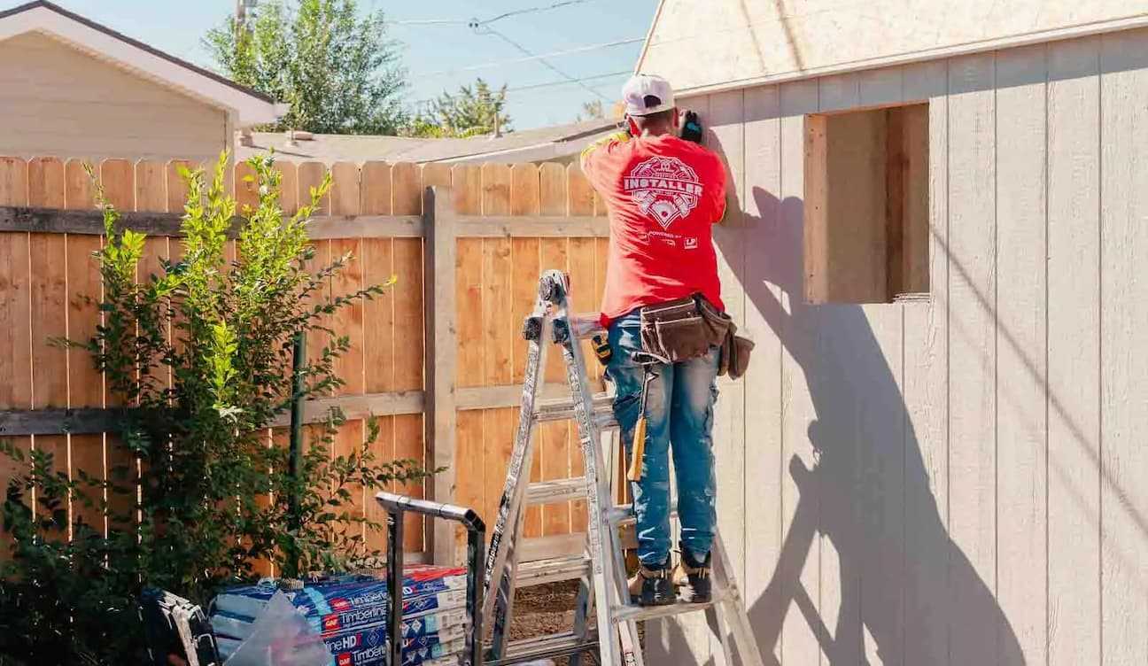 installer standing on the latter and working on installing a roof of a tuff shed