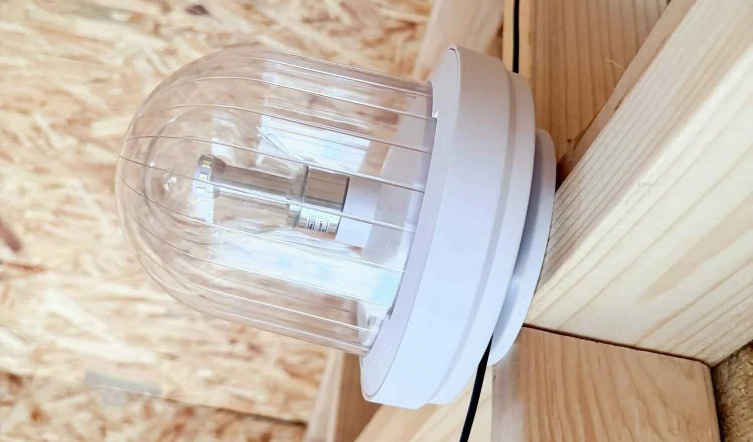 A clear dome-shaped light fixture mounted sideways on a wooden wall with a visible black cable.