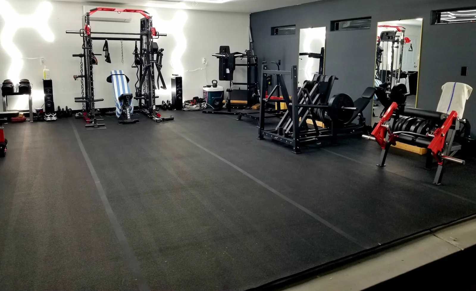Interior of Oliver's home gym with weight machines, mirrors, and lights