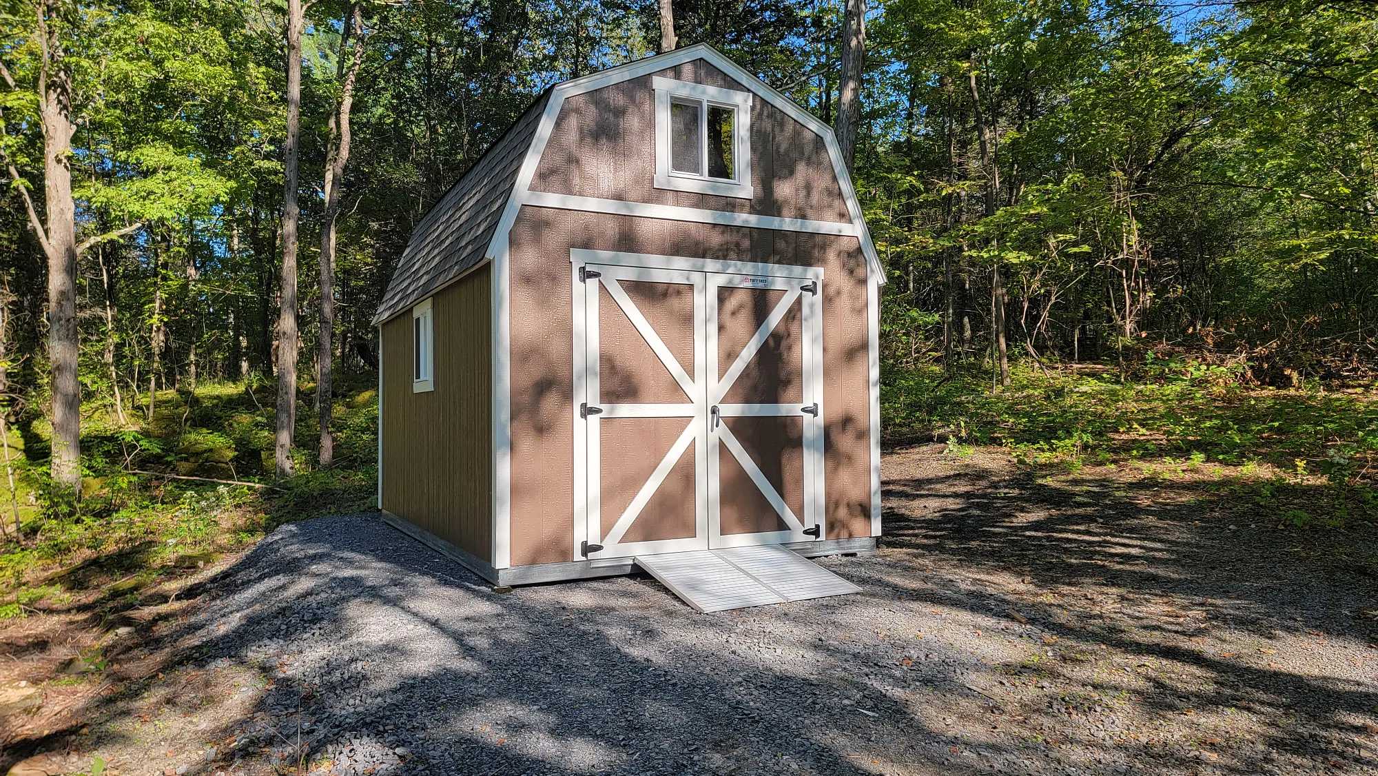Light brown and white barn in a forest with heavy duty steel ramps