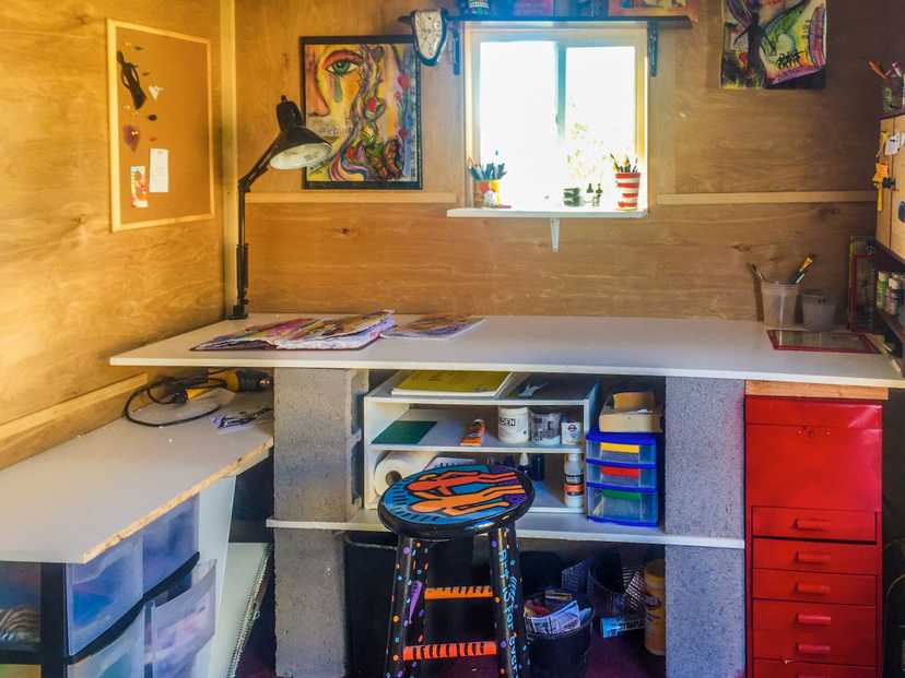 A premier lean to that has a desk and chair and art supplies all around it.