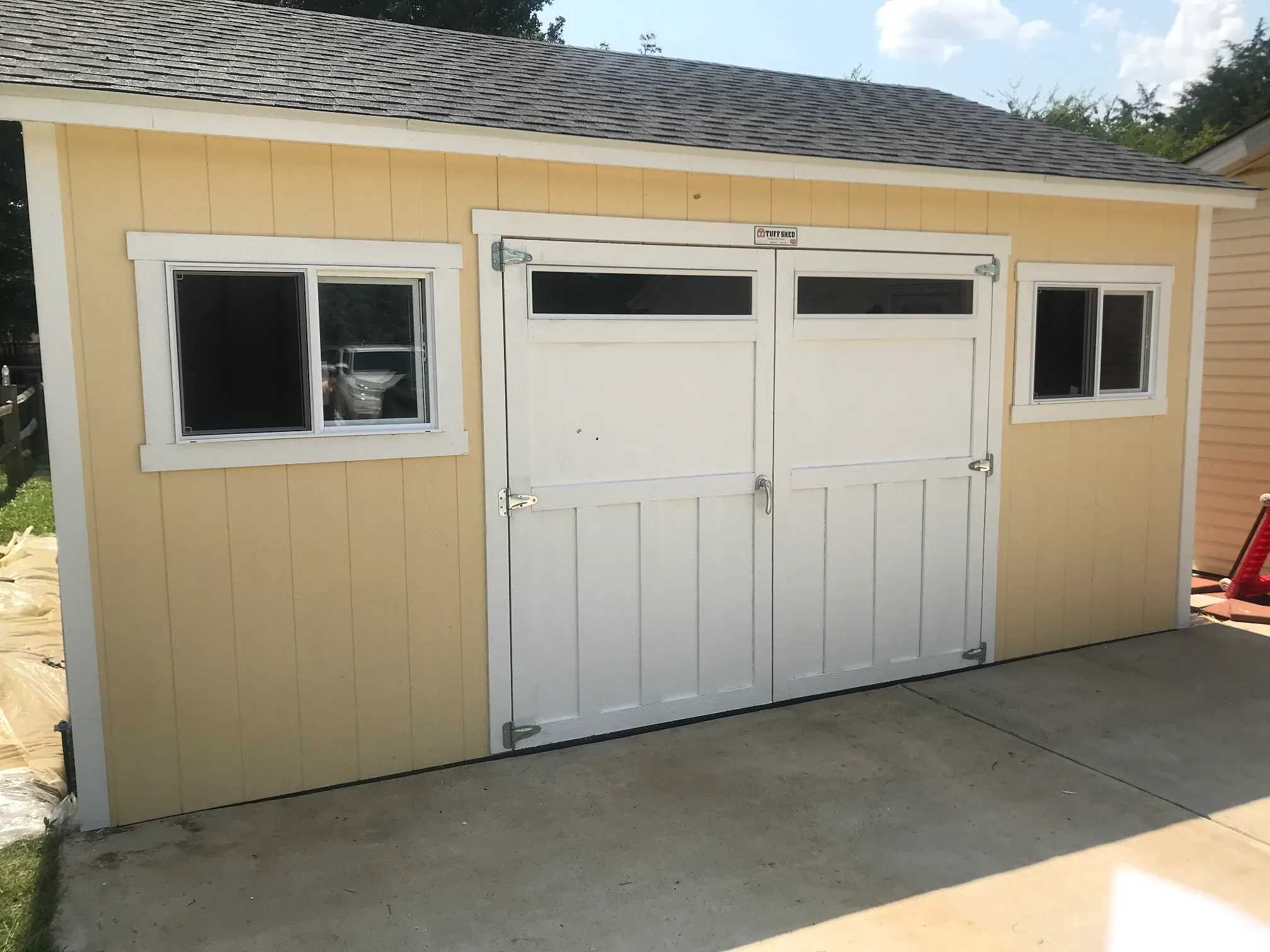 Yellow and white shed with double doors in a backyard
