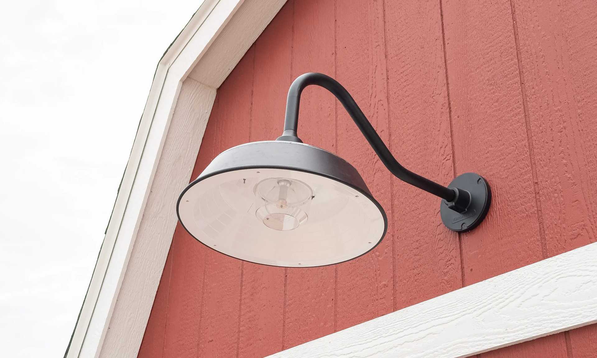 Black industrial-style wall lamp on a red wooden building exterior with white trim.