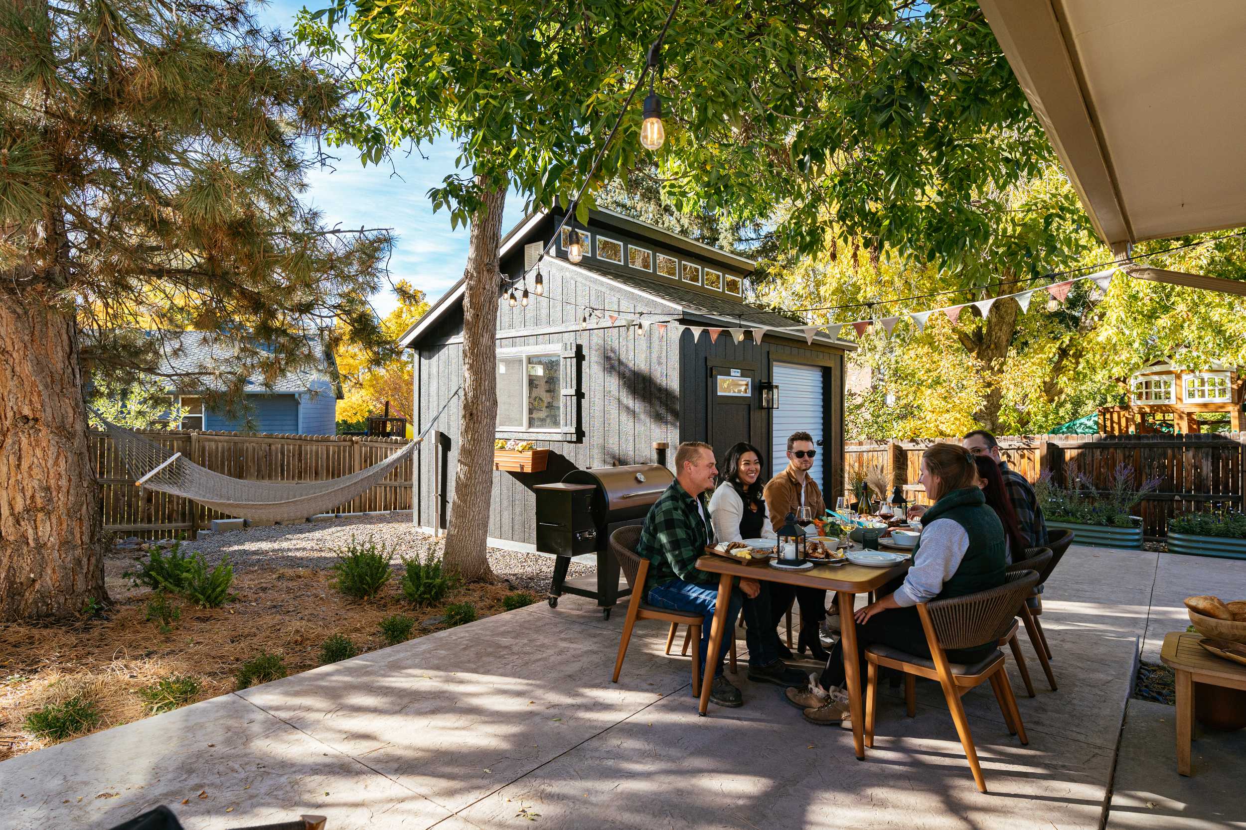 an outdoor patio set up with a shed on a background and group of people at the table enjoying dinner