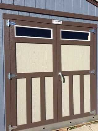 Exterior front of a blue shed with white and brown doors with in-the-door transom windows at top of doors