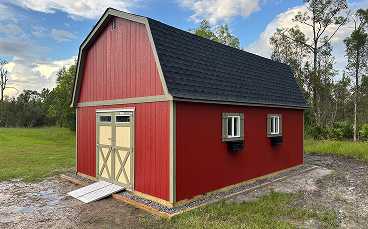 a red barn shed and black roof with double doors and two windows