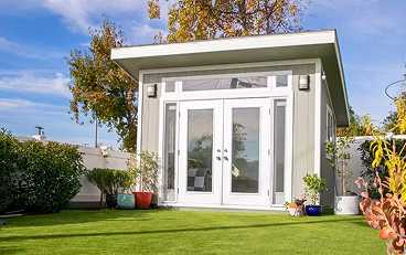 a white studio shed with double glass residential doors and transom door windows