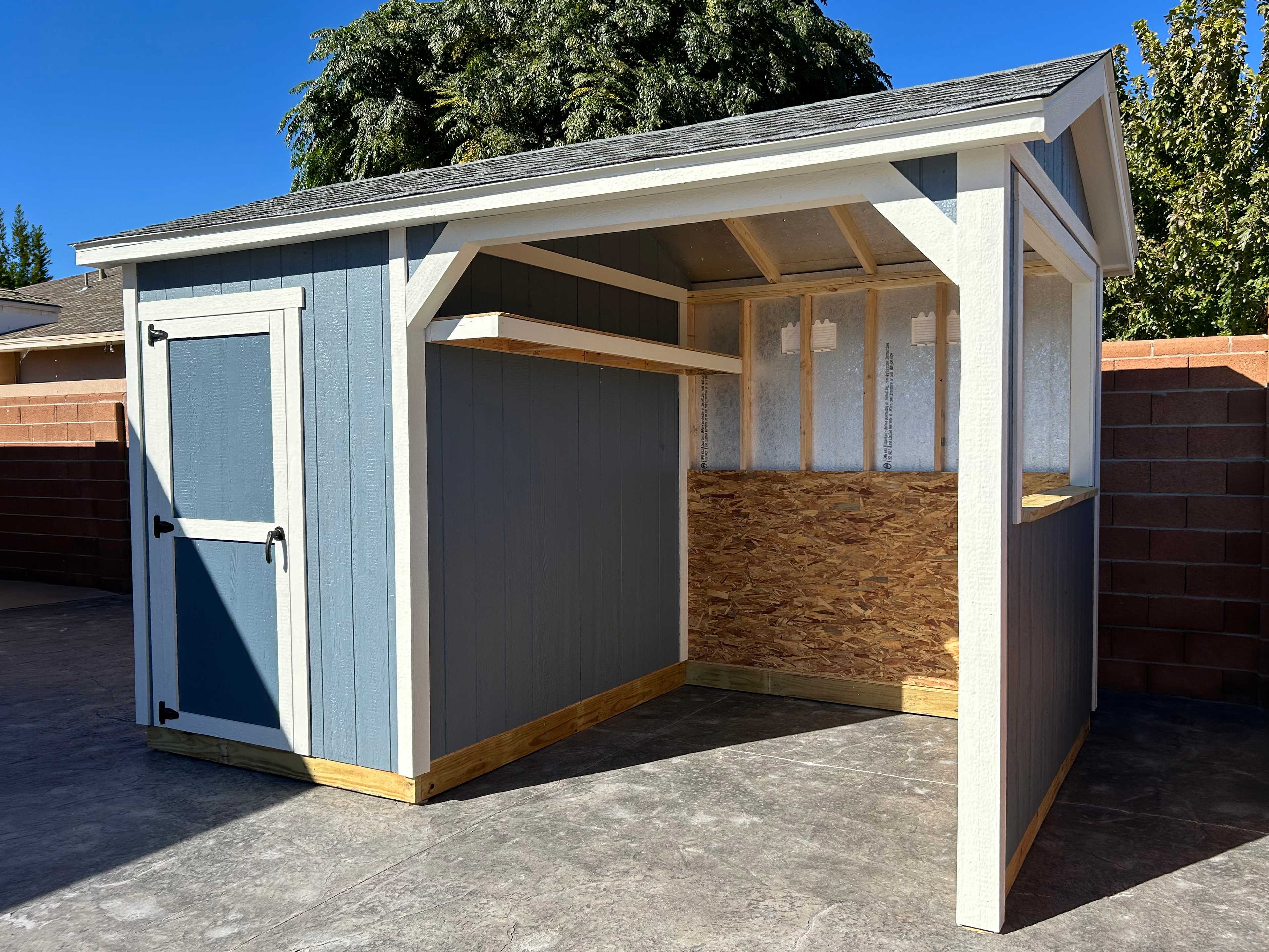 Blue loafing shed with white trim backed up against a brick wall