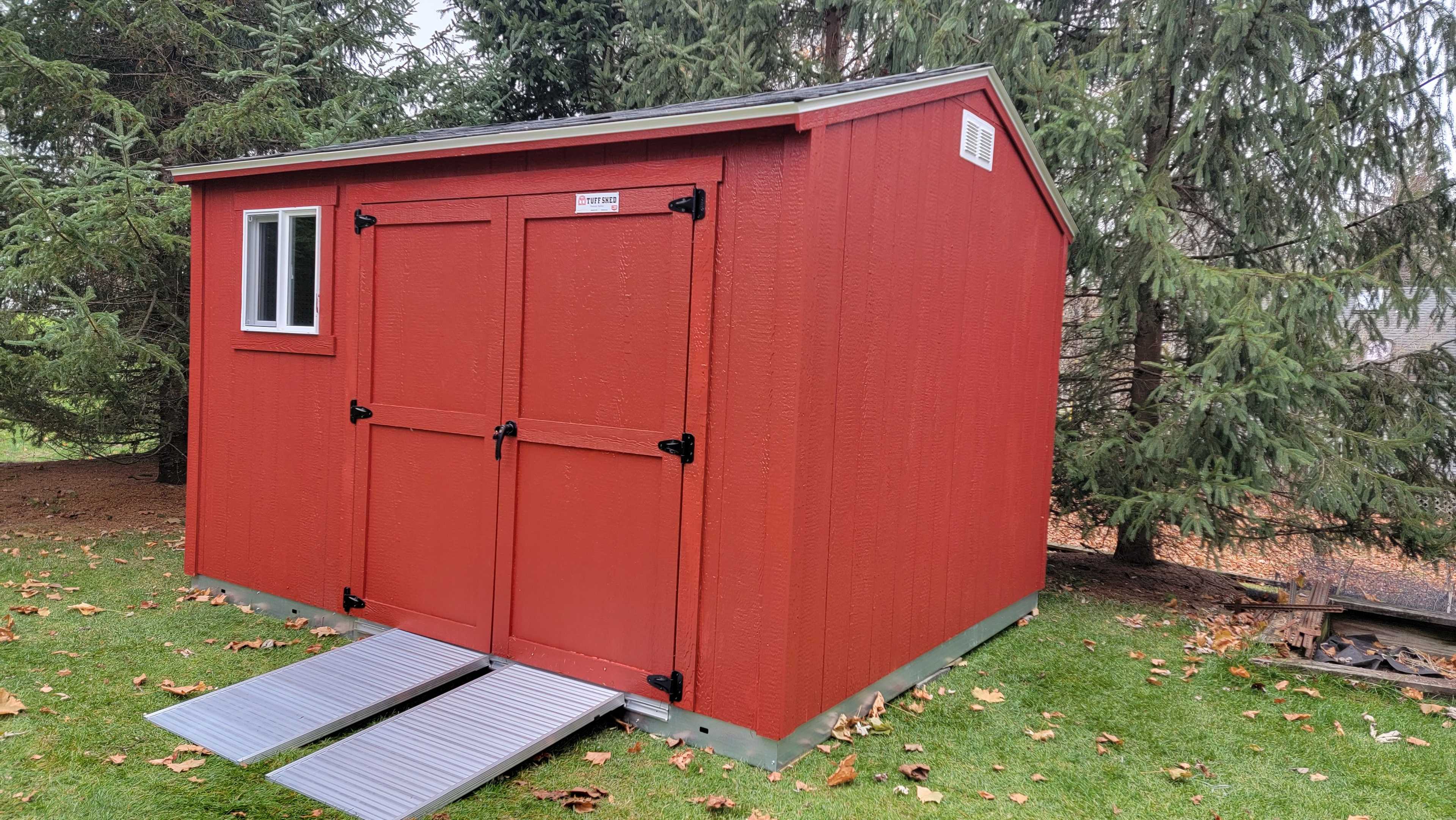 A red Premier Ranch featuring two metal ramps in a green yard with a white window