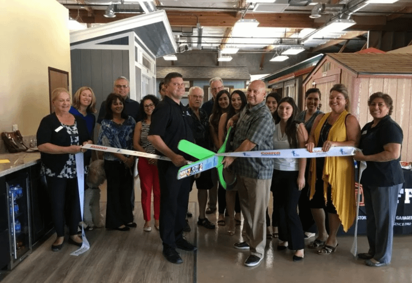 Interior of Thousand Palms Tuff Shed location with 16 people cutting a ribbon with giant green scissors in front of a shed display