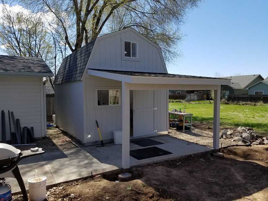 Big and white shed with a hang over cover in a yard.