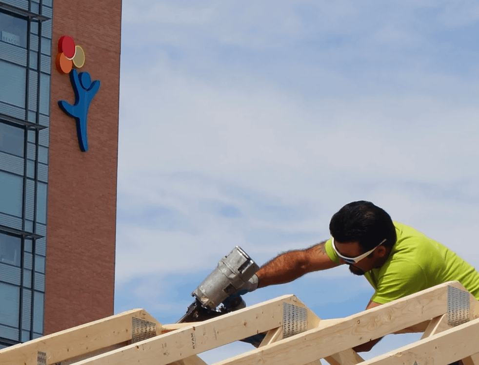 An exterior shot of an installer working on the trusses of a premier ranch garage with a nail gun, with the colorado children's hospital in the background